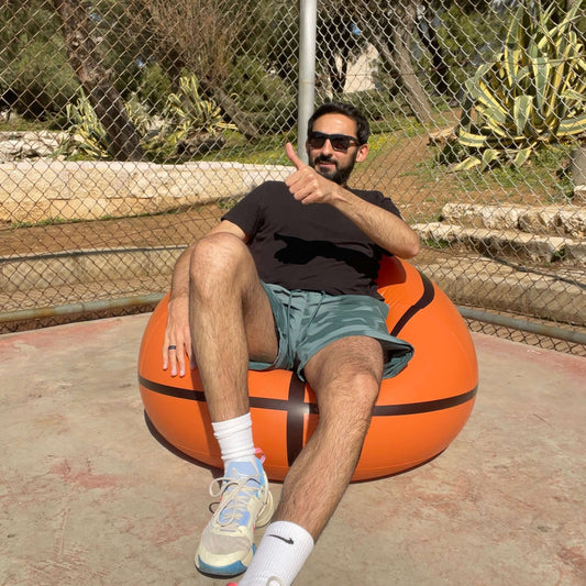 A person sitting on an Inflatable Basketball Sofa, enjoying court side comfort, wearing sunglasses and giving a thumbs up.